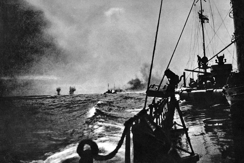 Pierwsze salwy bitwy jutlandzkiej. Rzuconą przez admirała Scheera rękawicę podjął dowódca floty brytyjskiej - admirał sir John Jellicoe. Admiralicja brytyjska, dzięki meldunkom wywiadu, zdawała sobie sprawę z planowanego przez Niemców podstępu. Wykorzystując tę wiedzę, zamierzała sama zaskoczyć przeciwnika. Funkcja harcownika przypadła admirałowi sir Davidowi Beatty, który miał związać okręty niemieckie walką, a następnie wystawić na cel podążających za nim okrętów brytyjskich. Poprzez ten manewr chciano doszczętnie rozbić siły niemieckie. Pierwsza faza bitwy (późnym popołudniem 31 maja 1916 roku), choć przyniosła Anglikom ciężkie straty, została przez nich sprawnie rozegrana, gdyż wyprowadziła główne siły niemieckie pod lufy nadciągającej flotylli admirała Jellicoe. Pierwsze salwy bitwy jutlandzkiej. Rzuconą przez admirała Scheera rękawicę podjął dowódca floty brytyjskiej - admirał sir John Jellicoe. Admiralicja brytyjska, dzięki meldunkom wywiadu, zdawała sobie sprawę z planowanego przez Niemców podstępu. Wykorzystując tę wiedzę, zamierzała sama zaskoczyć przeciwnika. Funkcja harcownika przypadła admirałowi sir Davidowi Beatty, który miał związać okręty niemieckie walką, a następnie wystawić na cel podążających za nim okrętów brytyjskich. Poprzez ten manewr chciano doszczętnie rozbić siły niemieckie. Pierwsza faza bitwy (późnym popołudniem 31 maja 1916 roku), choć przyniosła Anglikom ciężkie straty, została przez nich sprawnie rozegrana, gdyż wyprowadziła główne siły niemieckie pod lufy nadciągającej flotylli admirała Jellicoe.